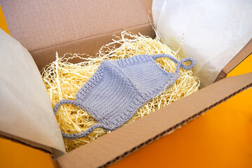 Knitted gray face mask in an open box on a yellow background. Home delivery. 