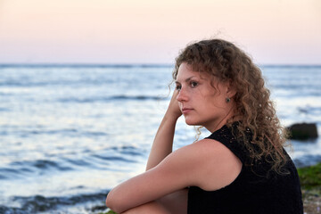 Fototapeta na wymiar A thoughtful woman sits alone on the sea beach near the water.