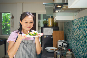 Asian woman holding  tasty cook dishes in the kitchen.
