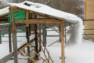 Animal shed. White snow is sliding from the roof. The concept of a village, farm, ranch in winter.