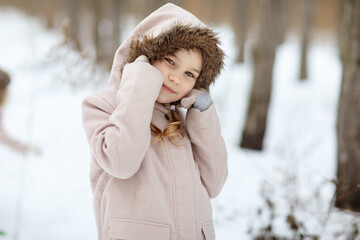 a little girl in the hood in a snowy winter forest. travel and recreation with children in winter. walking in the fresh air during the new year holidays.