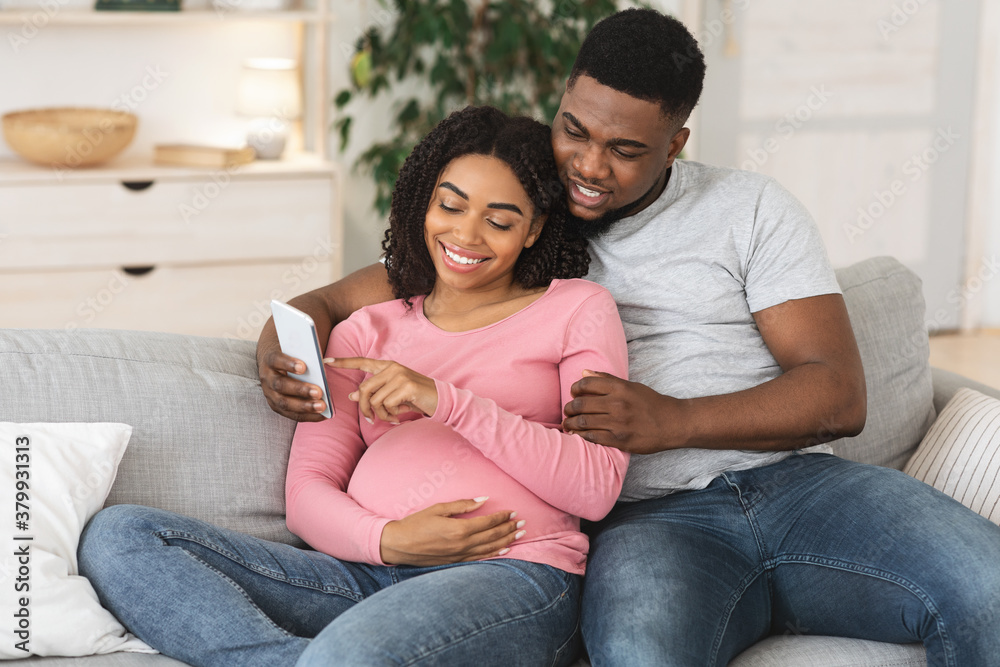 Wall mural pregnant black couple using smartphone together at home