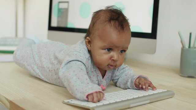 Lockdown of cute baby girl is lying on desk and playing with wireless keyboard