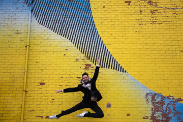 danseur en plein saut devant un mur de brique recouvert d'un immense graffiti en milieu urbain 