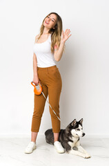Naklejka na ściany i meble A full length young pretty woman with her dog saluting with hand with happy expression