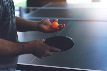 A young man is playing ping pong. He holds a ball and a racket in his hands