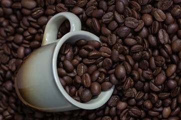 Coffee beans in light brown cup on the coffee beans background top view