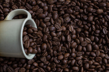 Coffee beans in light brown cup on the coffee beans background top view