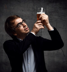 Man in stylish official clothing jacket and shirt holds up a glass of drink craft beer and looks...