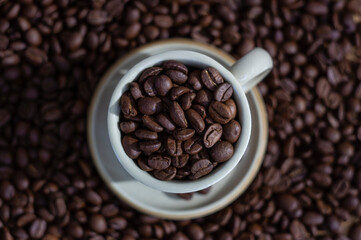 Coffee beans in light brown cup on the coffee beans background top view