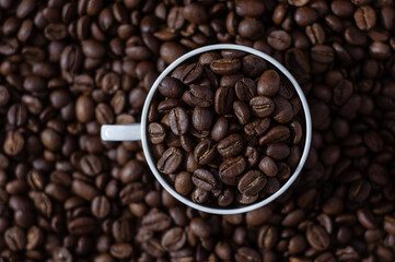 Coffee beans in white cup on the coffee beans background top view