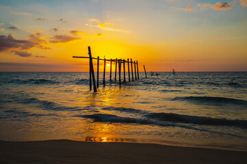 The view of the old wooden bridge decayed in the middle of the ocean in the evening. The sun is...