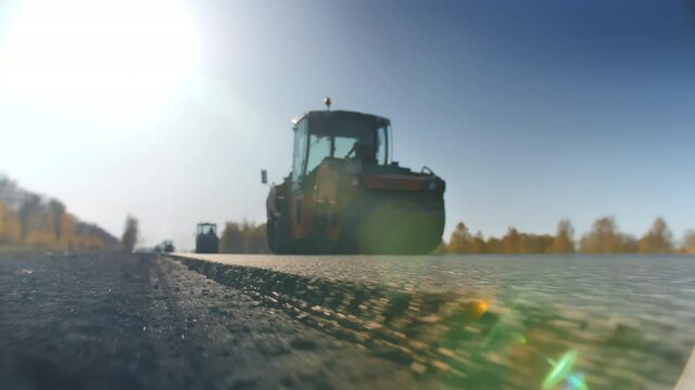 Shooting a layer of freshly laid asphalt. Road surface repair. Construction of a new road. The rollers levels and compacts the asphalt. Road rollers. Sun glare.