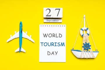 Happy world tourism day. Touristic decorative items, plane and vessel on bright yellow background. Flat lay, top view. Calendar date September 27, notebook with text WORLD TOURISM DAY