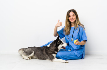 Veterinary doctor with Siberian Husky dog sitting on the floor giving a thumbs up gesture