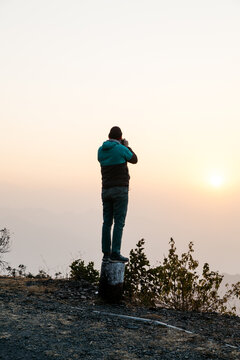 young male photographer taking photo in nature landscape at sunrise