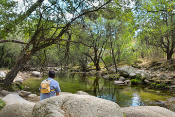 A hiker rests by the backwater of a mountain stream enjoying the peaceful scenery. "Sierra de Guadarrama" National Park, Madrid, Spain