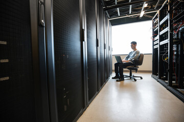 Distant view of technician working on laptop in server room