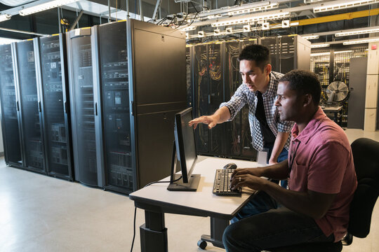 Wide angle of two technicians talking while looking at computer