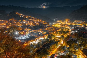 Fototapeta premium GUIZHOU, CHINA - APRIL 17: Xijiang miao village, largest village in Guizhou Miao ethnic minority, April 17, 2010. Night illumination of houses and bridge over river village in Xijiang. Leishan County.