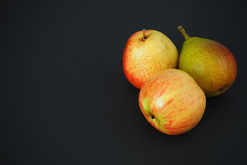 Beautiful pears and an apple on a black background. Ripe