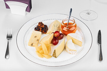 Cheese plate dairy meal assortment with honey, walnut and grapes.
