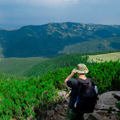 Fototapeta premium A tourist with a black backpack looks into the distance high in the mountains