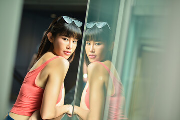 Beautiful young asian woman wearing sunglasses on head and looking camera standing near window.