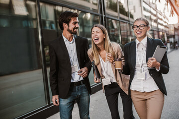 Three cheerful young business people talking to each other while walking outdoors