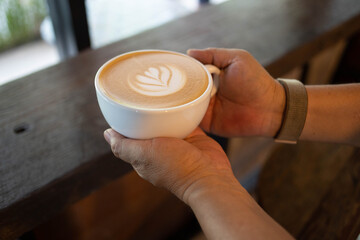 Fototapeta na wymiar Hand put a Latte arts coffe hot coffee on wooden table.barista love art concept.