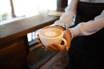 Hand put a Latte arts coffe hot coffee on wooden table.barista love art concept.