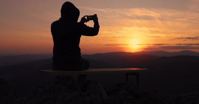 Man making photos of burning sunset sky and panoramic view of mountain hills