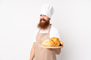 Redhead man in chef uniform. Male baker holding a table with several breads with happy expression
