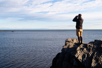Obraz premium Man standing on a cliff and looking through binoculars in the Bic national park, Canada