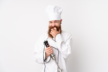 Redhead man using hand blender over isolated white background nervous and scared