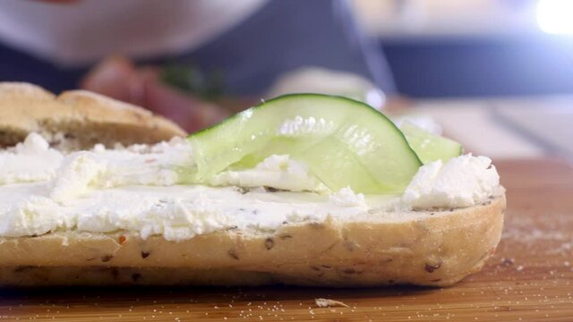 chef puts thin slices of fresh cucumber on crunchy bun prepare cheese sandwich. Making homemade ham baguette sandwich with cheese in kitchen. Morning Breakfast and lunch. Fast food in a restaurant.