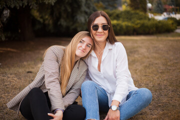 two beautiful, young, attractive, cheerful friends are sitting in the park on the grass