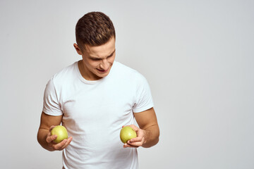 a guy with apples in his hands on a light background in a white t-shirt gesticulate with his hands...