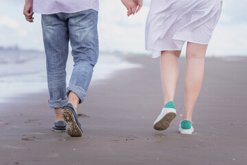 male and female legs in sports shoes walk along the beach against the background of the sea.