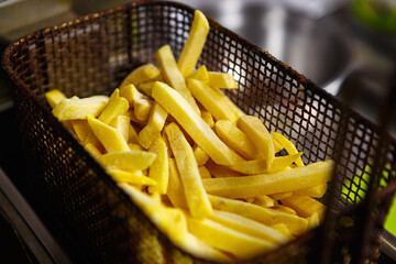 Raw uncooked french fries in deep fryer oven in fast food restaurant kitchen.Delicious frozen potato chips ready for cooking in fastfood diner.Fry potatoes preparation for dinner in cafe