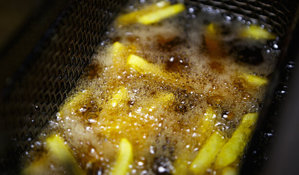 French fries frying in deep fryer in hot oil.Kitchen in American fast food restaurant cooking potato chips for dinner meal.Golden potatoes sticks being fried in deep-fryer friture oven in cafe