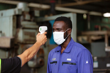 Fototapeta na wymiar Factory industry worker using infrared forehead thermometer scan at head with African American man worker in front of the warehouse at the factory during coronavirus outbreak