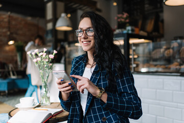 Satisfied female freelancer surfing cellphone in cafeteria
