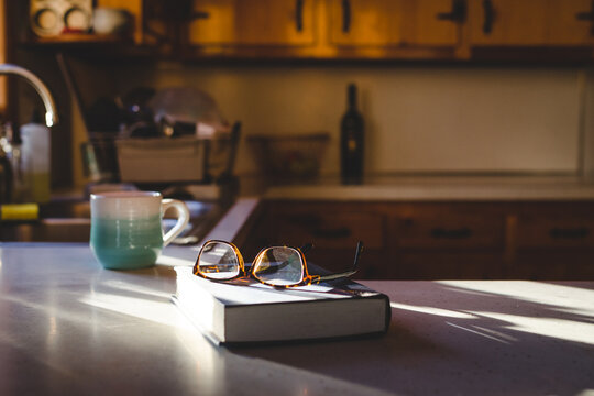 Glasses, book, and coffee mug sitting on a sunny kitchen counter