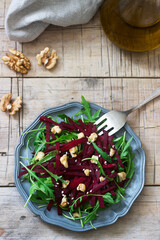 Vitamin salad of raw beets, arugula, walnuts and olive oil on a wooden table. Rustic style.