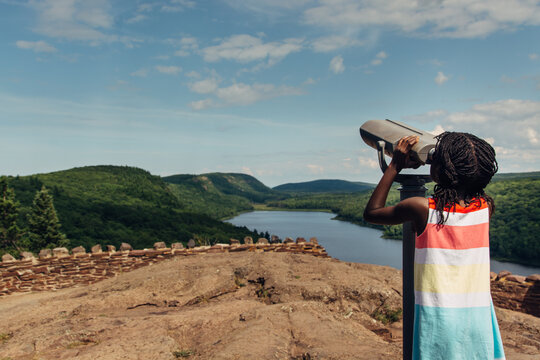 Black girl looking through a tower viewer in a scenic hilly plac