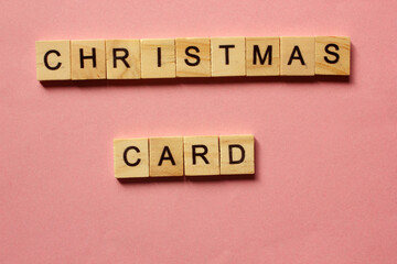 Words Christmas Card. Wooden blocks with inscription on pink background. The bulletin board. Concept of holiday-Christmas and New year. View from above. Copy space for text. Christmas and New Year.