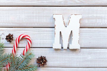Wooden letter M on white wooden background decorated with spruce branches, pine cones and New...