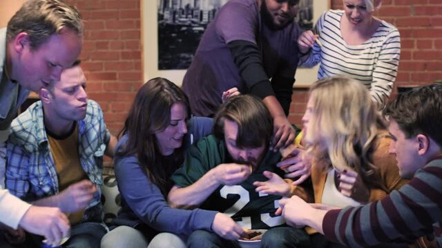 WS of a group of friends sitting on a couch fighting over who gets to dip their chip in salsa.