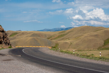 Asphalt serpentine mountain road against the background of undulating mountains, picturesque sky with clouds